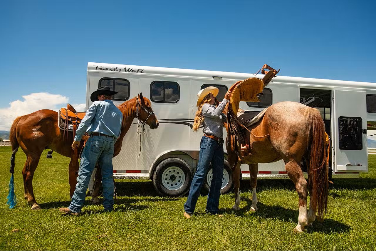 Horse owners with their horses beside a horse trailer in a field